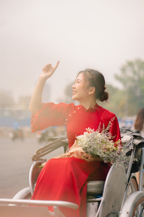 Young Woman in a Red Dress Sitting in a Carriage and Holding Flowers