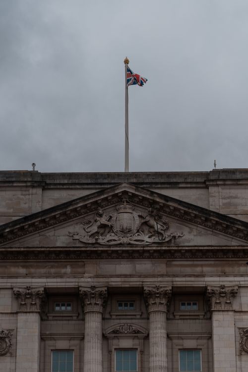 Free Low angle shot of Buckingham Palace with overcast skies, highlighting its architectural details and British flag. Stock Photo