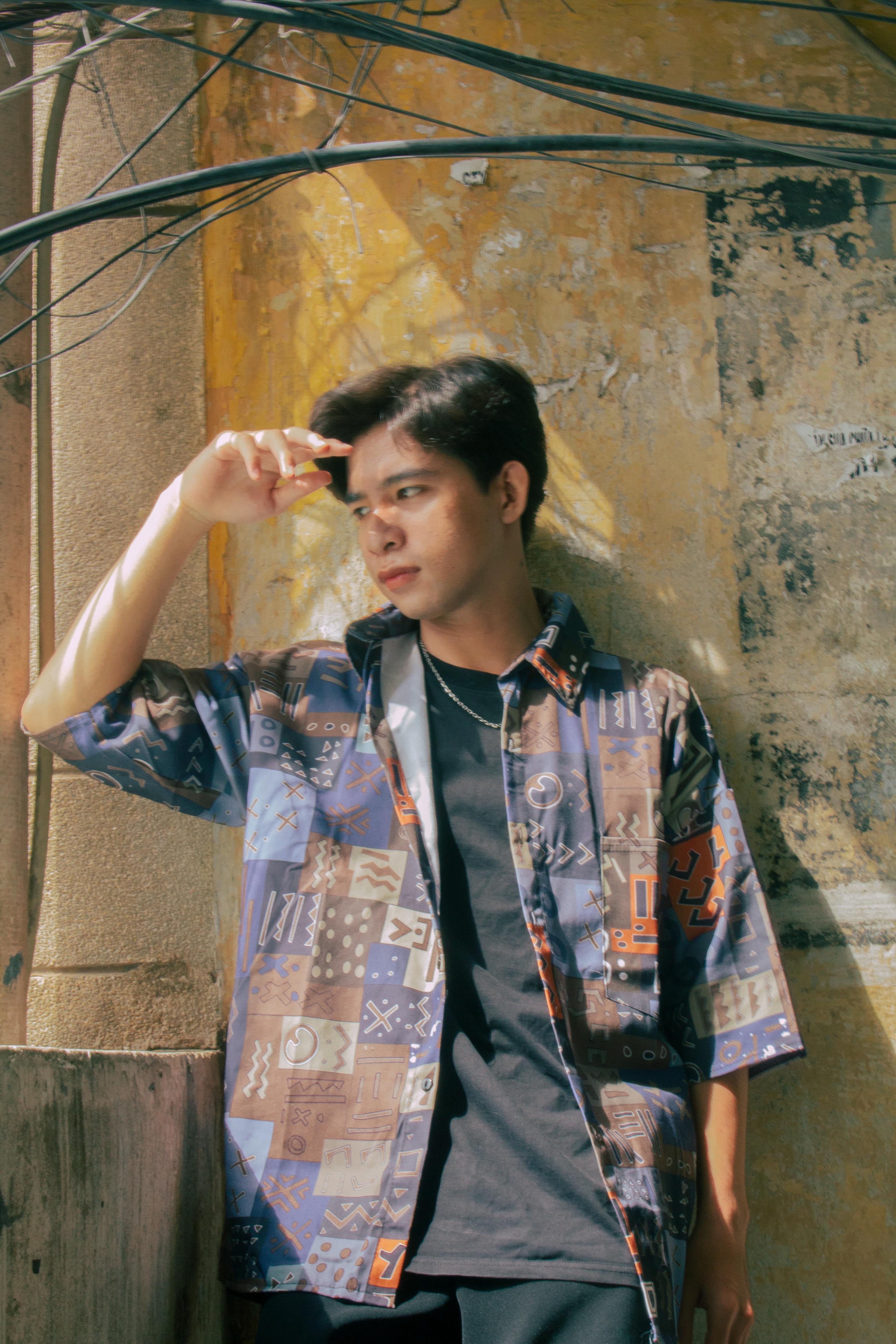 a young man leaning against a wall wearing a shirt