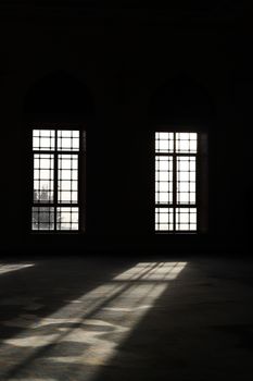 Dramatic sunbeams cast through large vintage windows of an empty room.