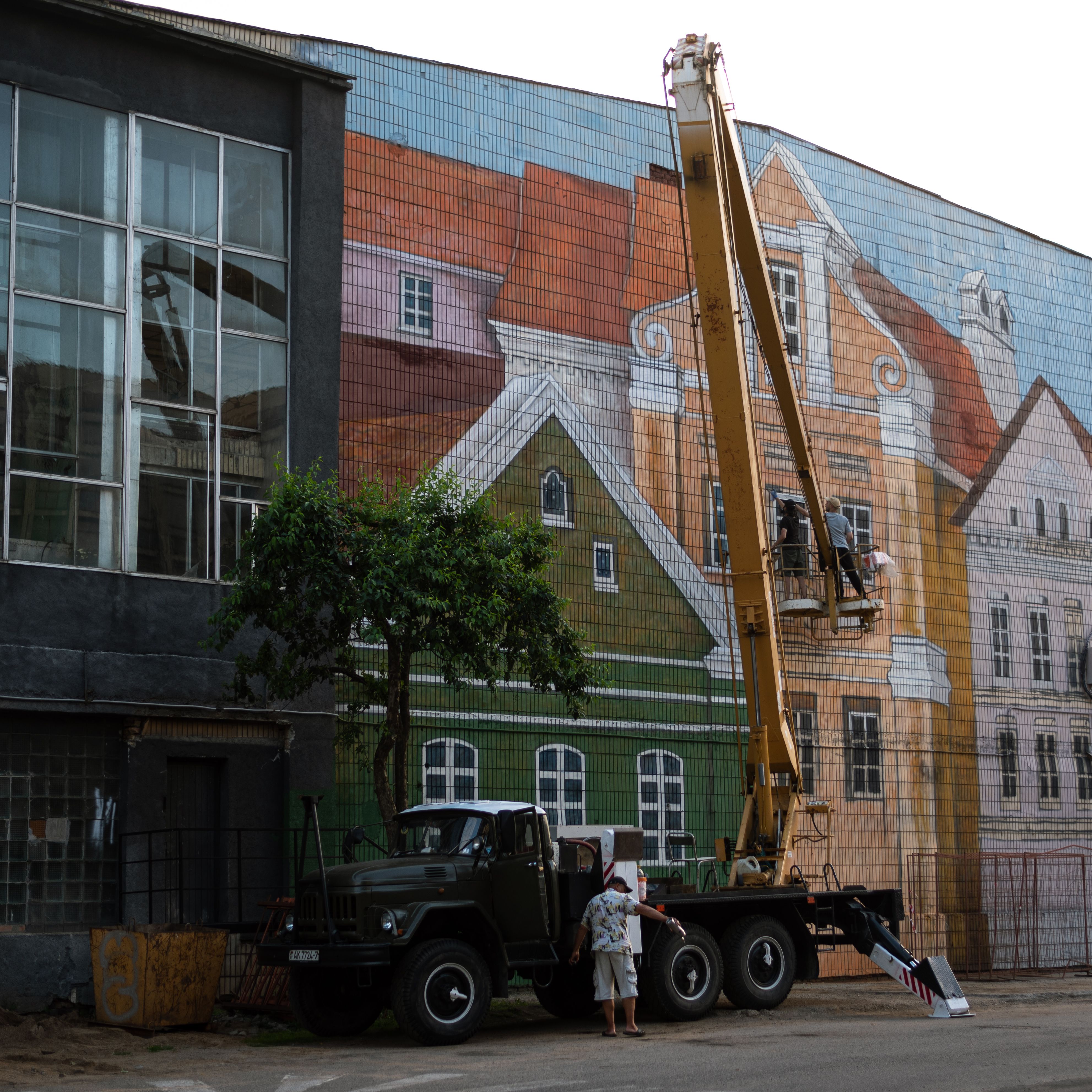 A large crane near a vibrant mural on a city building. Urban artistic transformation.