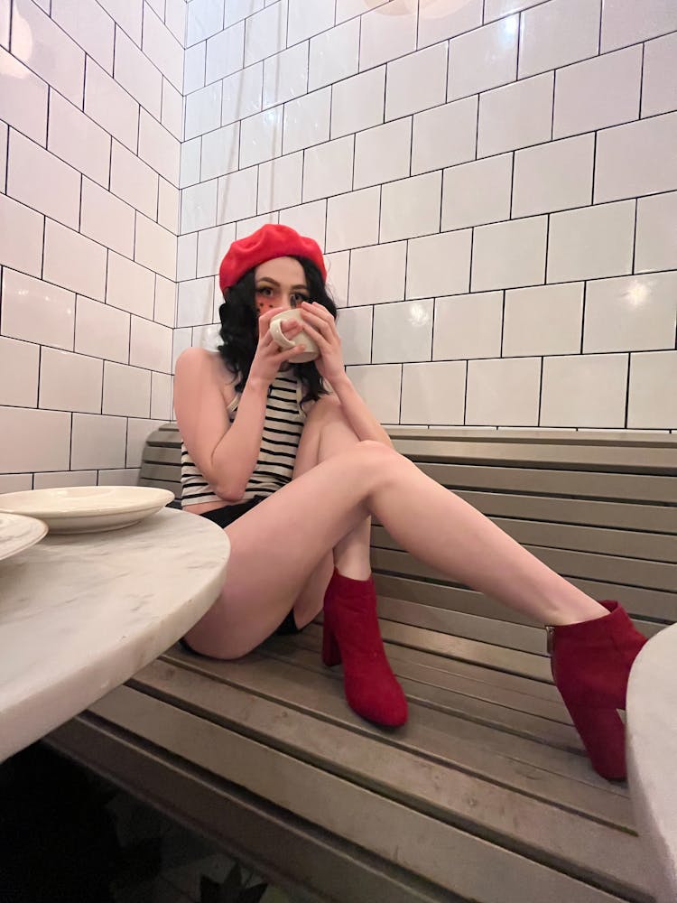 Young Woman In A Red Beret Drinking Coffee On A Bench In A Cafe