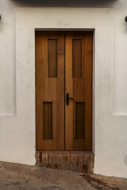 A modern wooden door set against a minimalist white wall on a city street.