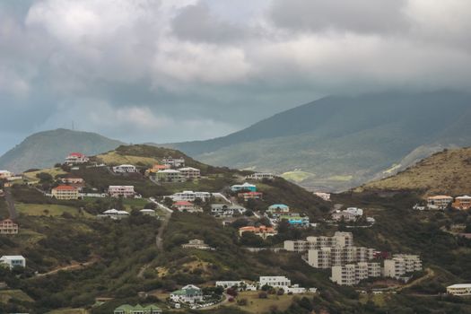 A picturesque view of a residential area nestled in lush green hills with a backdrop of towering mountains.