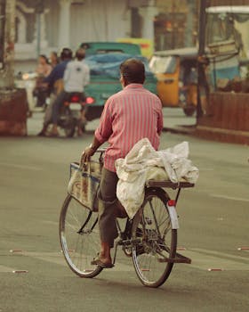 An adult man riding a bicycle on a bustling city street, capturing everyday life in India.