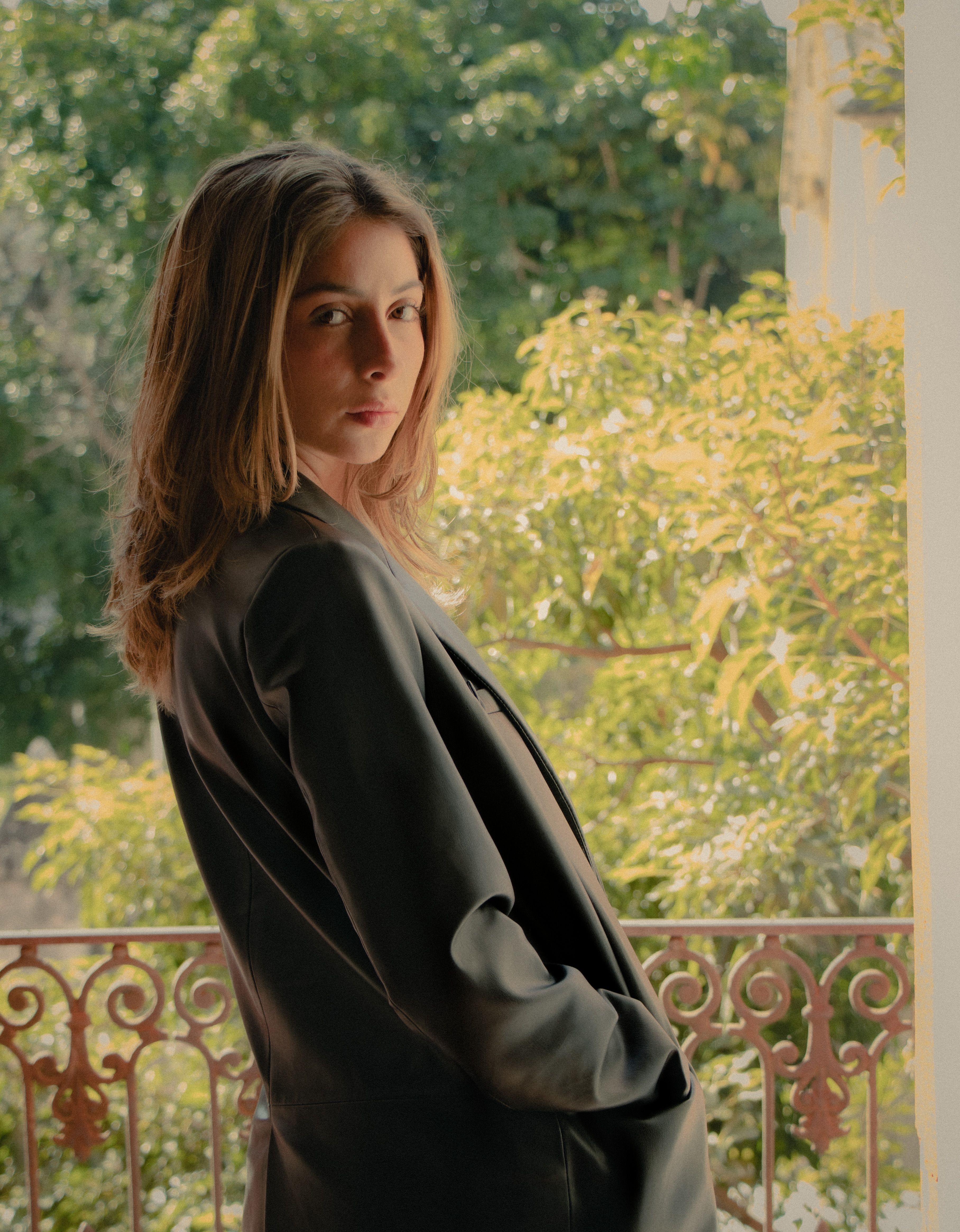 Portrait of a young woman in a gray blazer posing on a balcony with lush greenery in Ciudad de México.