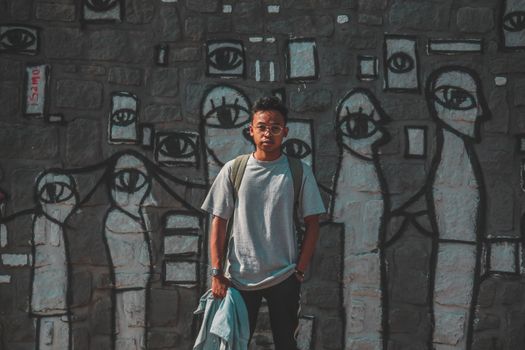 A young man stands confidently before a vibrant graffiti mural, captured outdoors during the day.