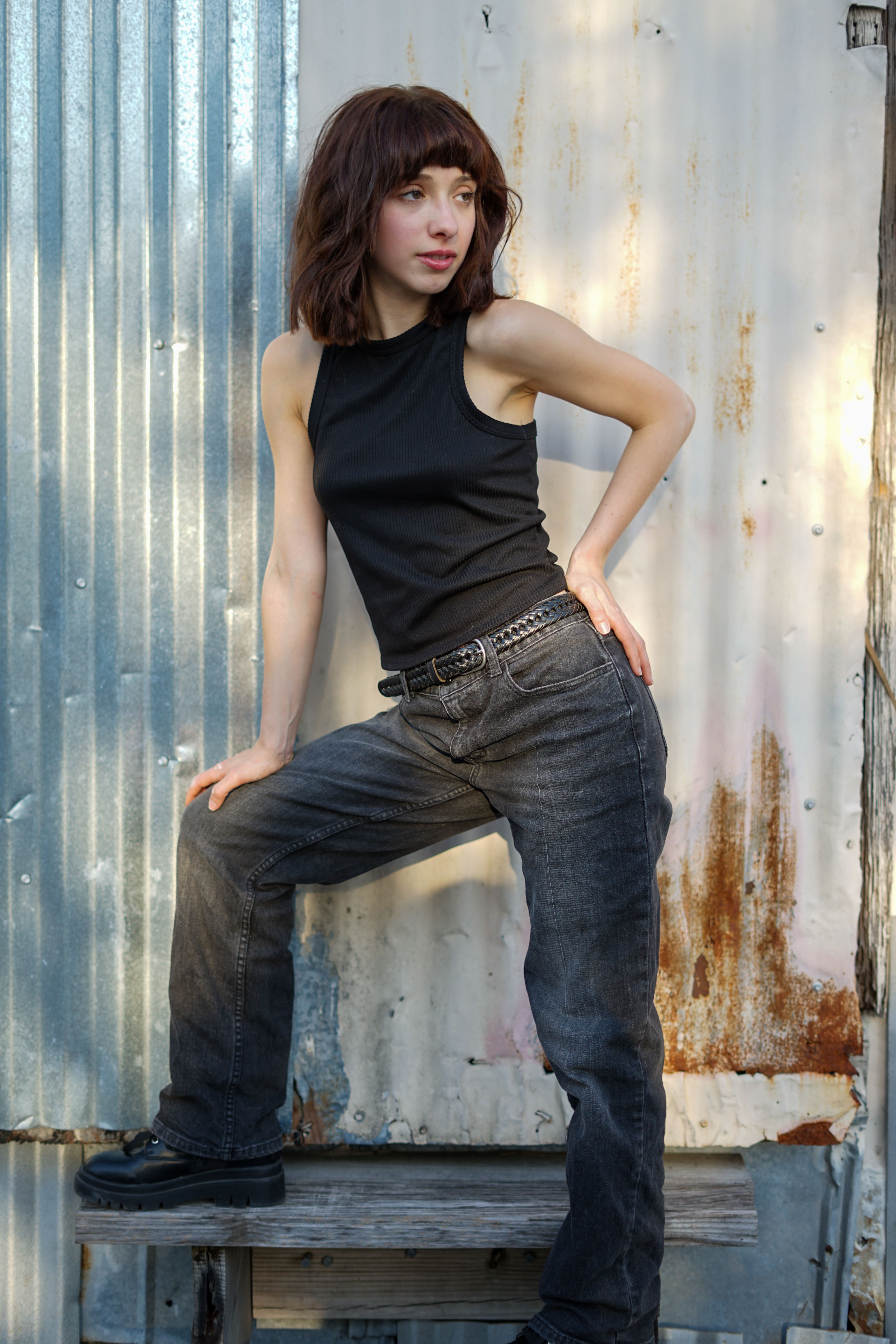 A modern portrait of a woman standing confidently in jeans and a tank top outdoors.