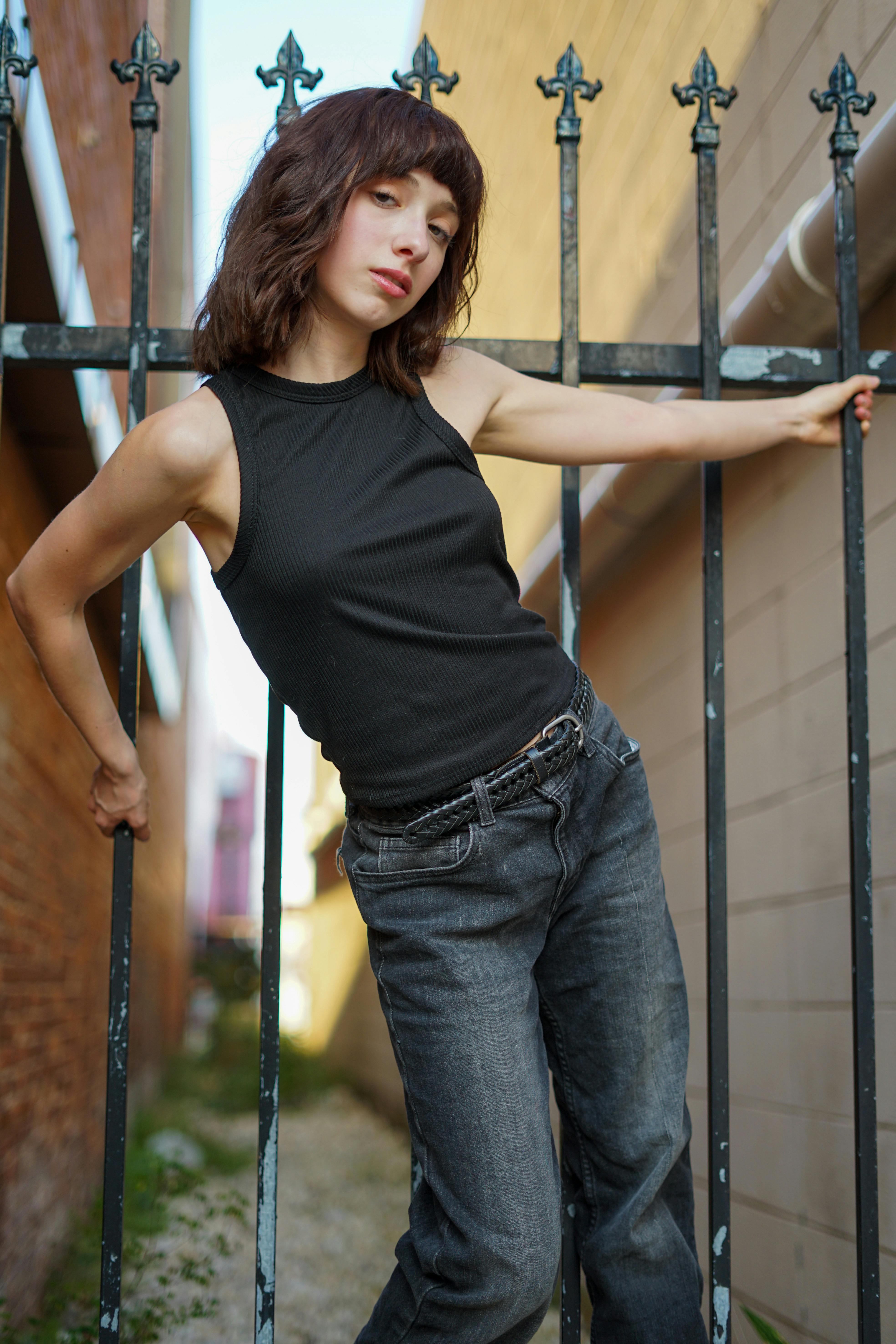 Confident woman in casual attire posing against an iron fence in an urban setting.