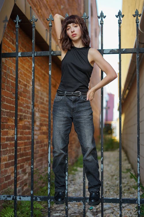 Young Woman in a Black Top and Jeans Standing on a Metal Fence 
