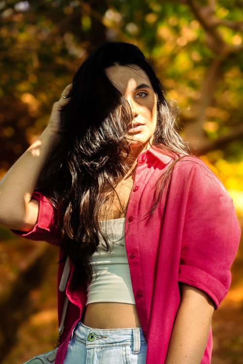 Free A woman with long dark hair poses outdoors in a pink shirt and casual attire. Stock Photo