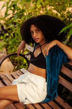 A fashionable woman with curly hair sitting on a bench, enjoying a sunny day.
