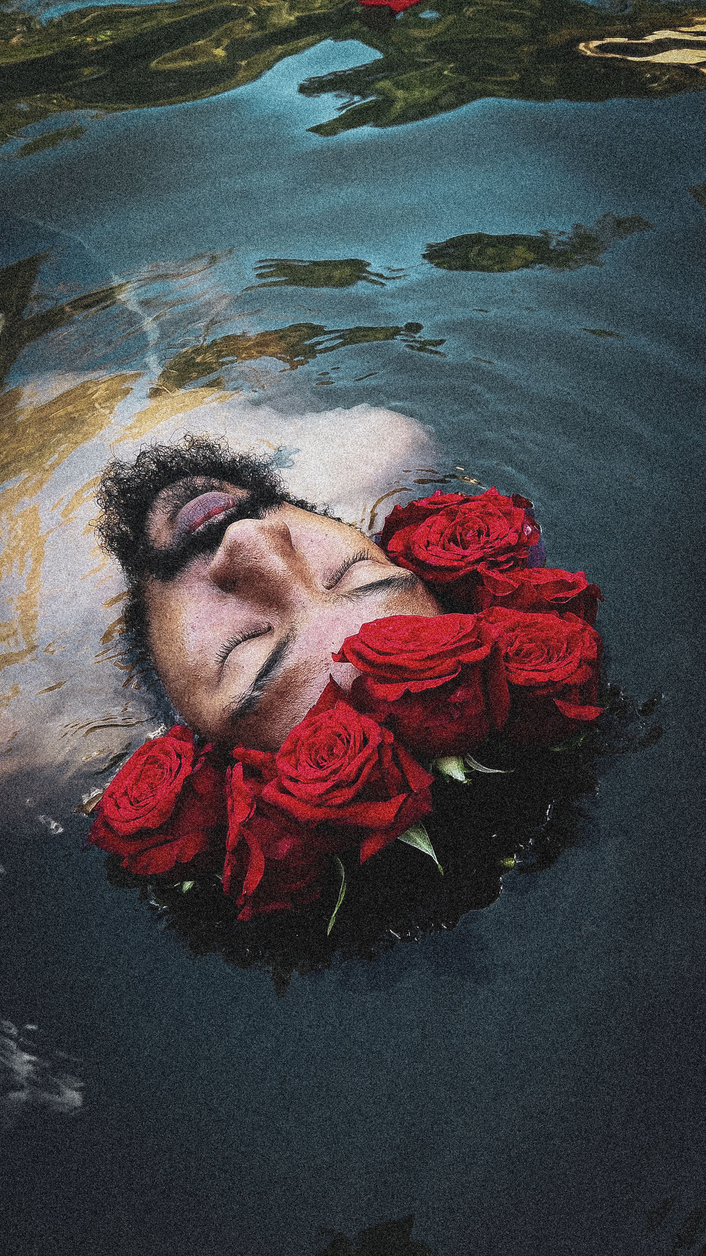 A man with eyes closed, floating in water wearing a wreath of red roses in Canóvanas, Puerto Rico.