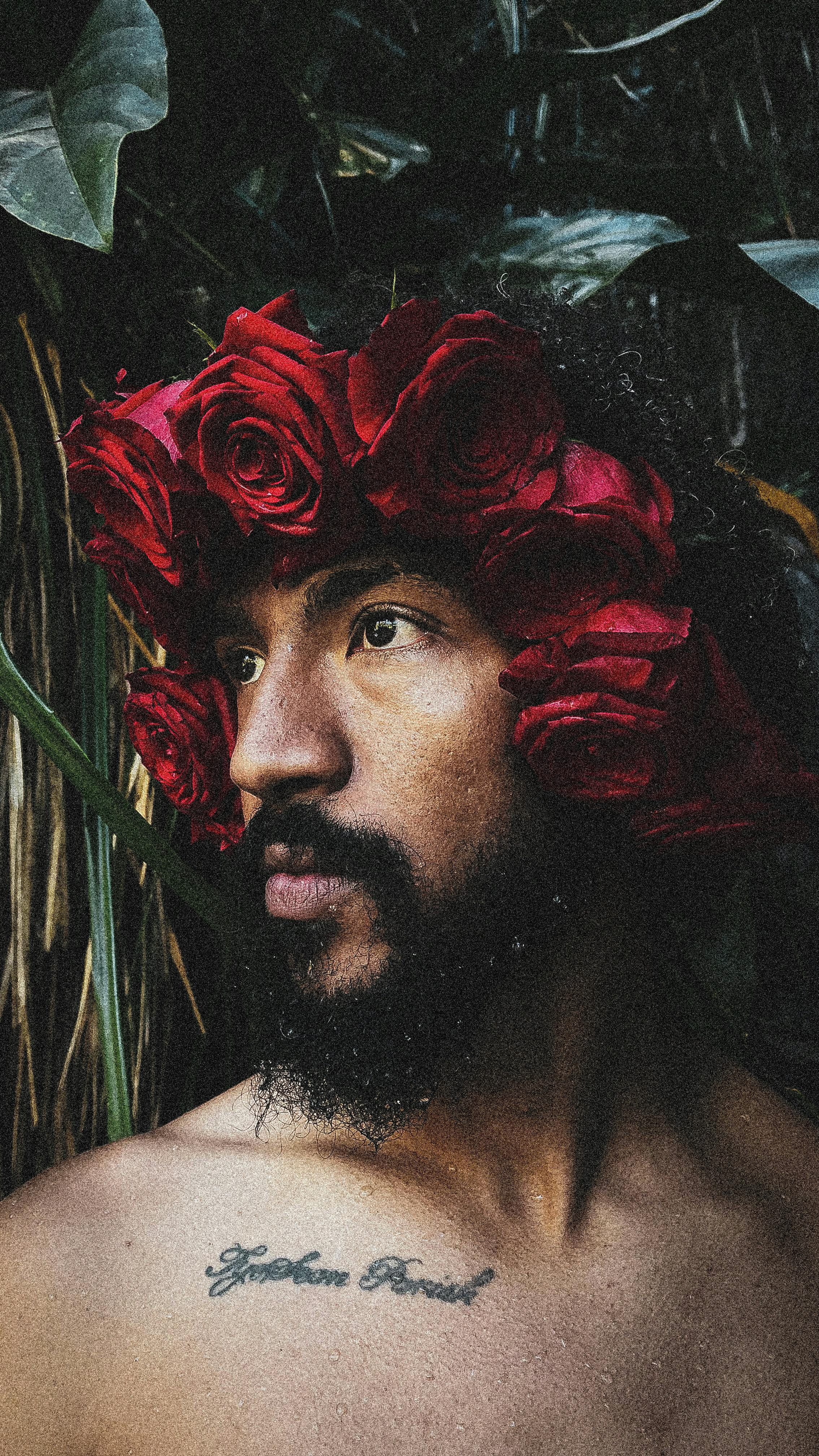 Creative portrait of a man wearing a wreath of red roses, blending nature and fashion.