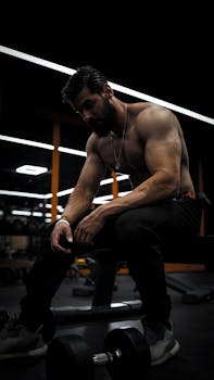 Topless muscular man with beard resting on a bench in Sulaymaniyah gym. Intense sports vibe.