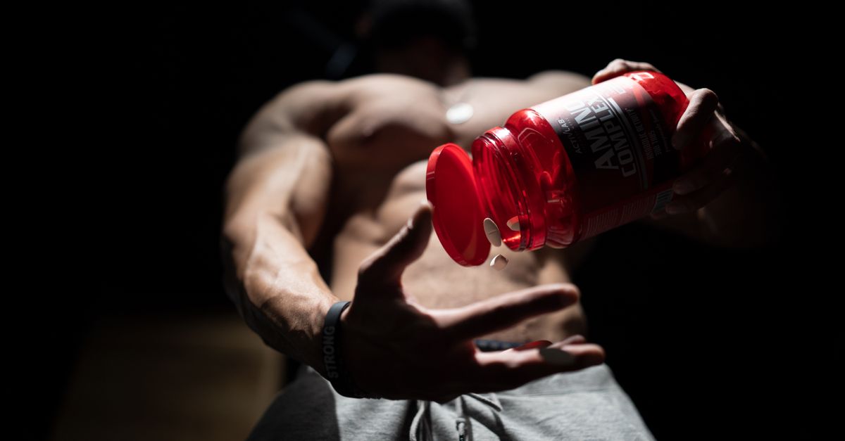 Shirtless muscular man pouring protein supplements from a bottle, showcasing fitness and strength. - Evidence evidence guide for branched chain amino acids muscle soreness randomized trial