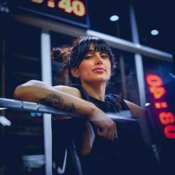 A youthful woman poses confidently in a gym, surrounded by fitness equipment.