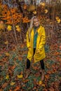 一位时尚女士穿着黄色雨衣，在鲜艳的秋叶中微笑