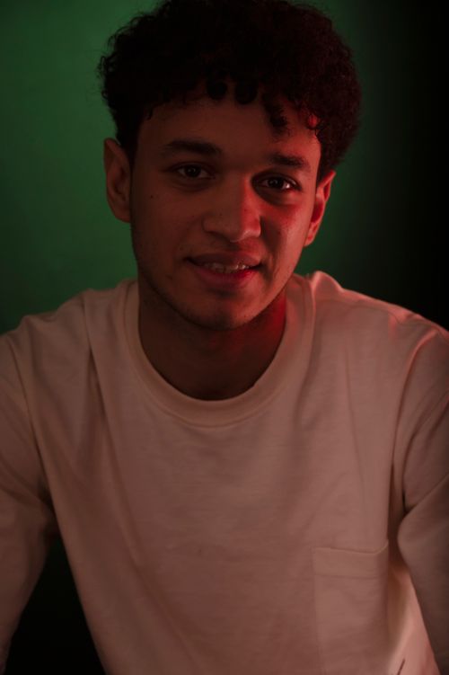 Free A portrait of a young man in a white shirt against a green background, enhanced by red lighting. Stock Photo