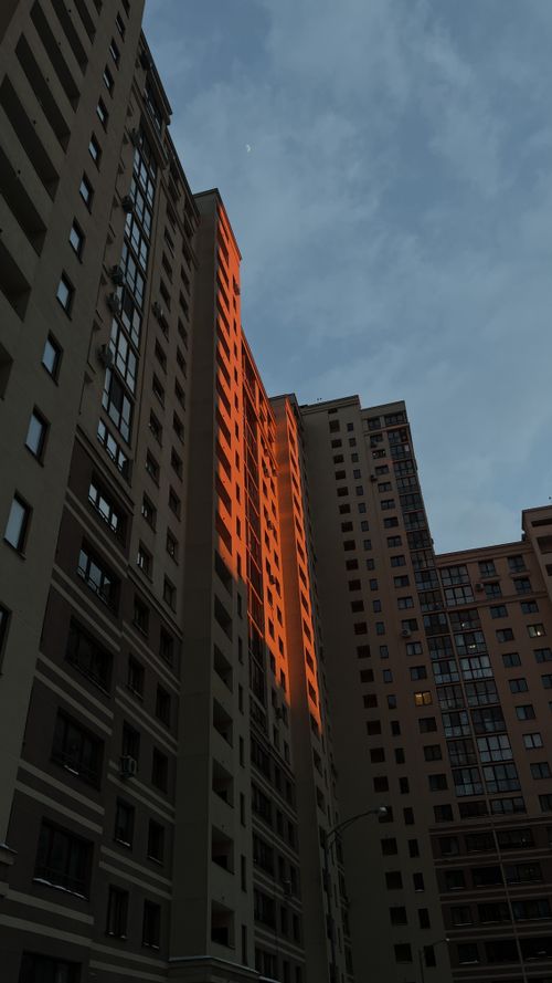 Free Tall apartment blocks with a warm sunset reflection under a cloudy sky. Stock Photo