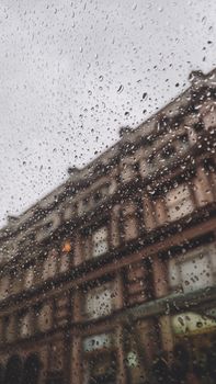 Blurred city building view through raindrop-covered window on an overcast day.
