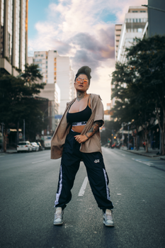 Stylish woman confidently poses in urban streetwear amidst city backdrop during the day.