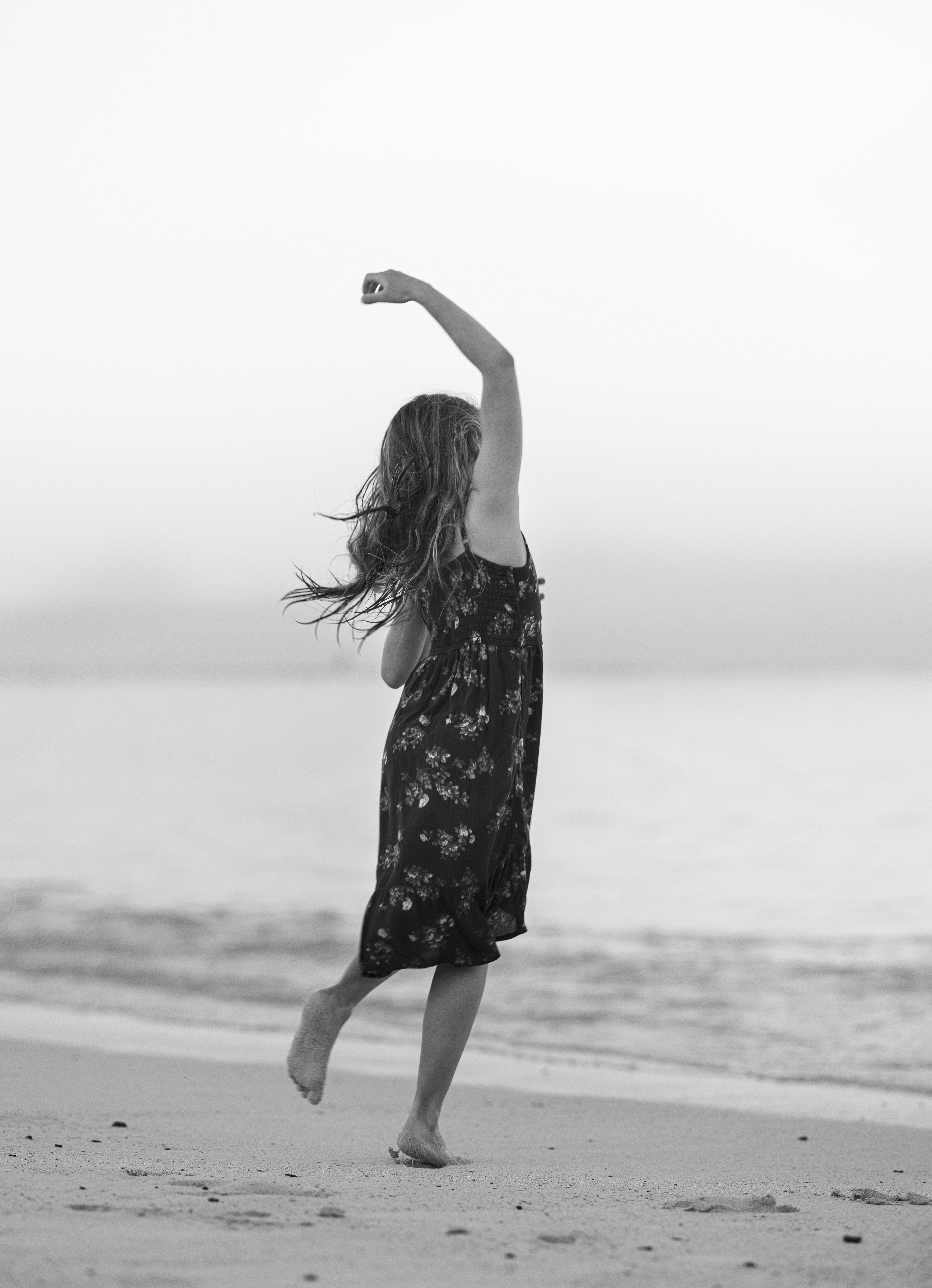 A young girl joyfully dancing on a serene beach, captured in black and white.