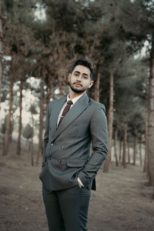 Free Portrait of a young man in a stylish suit standing confidently in a wooded area, exuding elegance. Stock Photo
