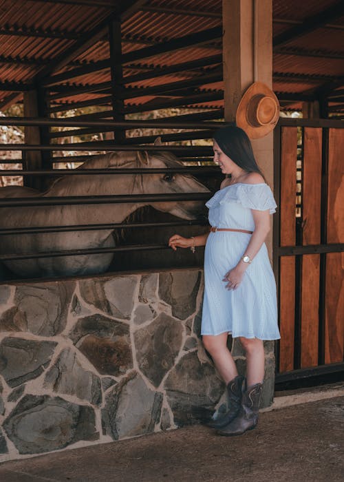 Woman in Blue Dress Standing near Horse at Stable