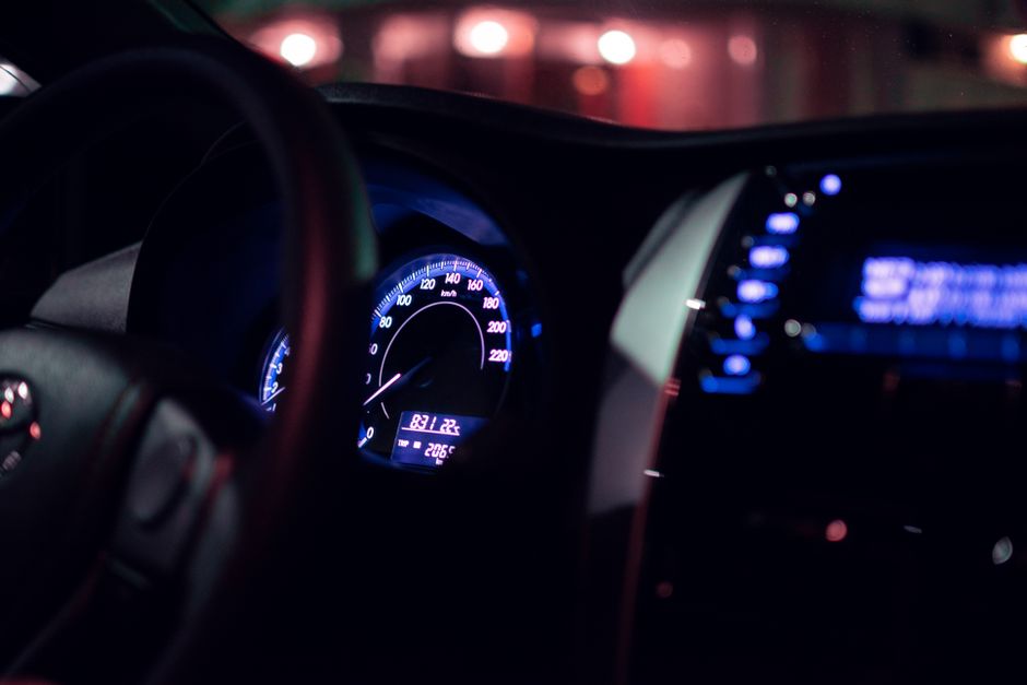 Close-up of a modern car dashboard at night, featuring illuminated speedometer and controls.