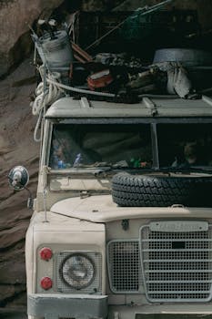 A vintage Land Rover packed for adventure, parked against a rocky background.