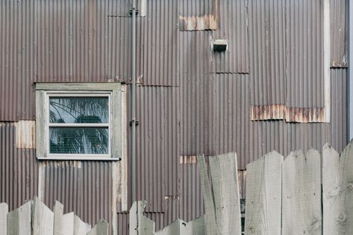 Free Aged corrugated metal wall with window and rustic wooden fence in rural setting. Stock Photo