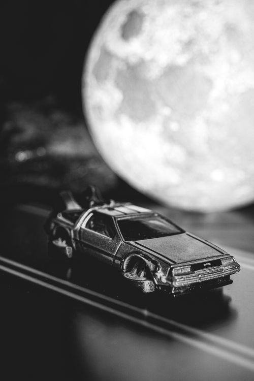 Free A grayscale close-up of a DeLorean model car against an illuminated moon backdrop. Stock Photo