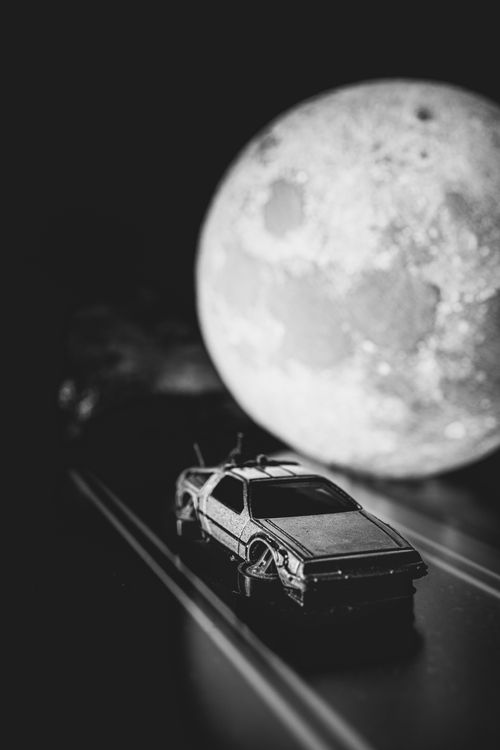 Free A black and white photo of a toy DeLorean under a full moon, evoking nostalgic, sci-fi vibes. Stock Photo