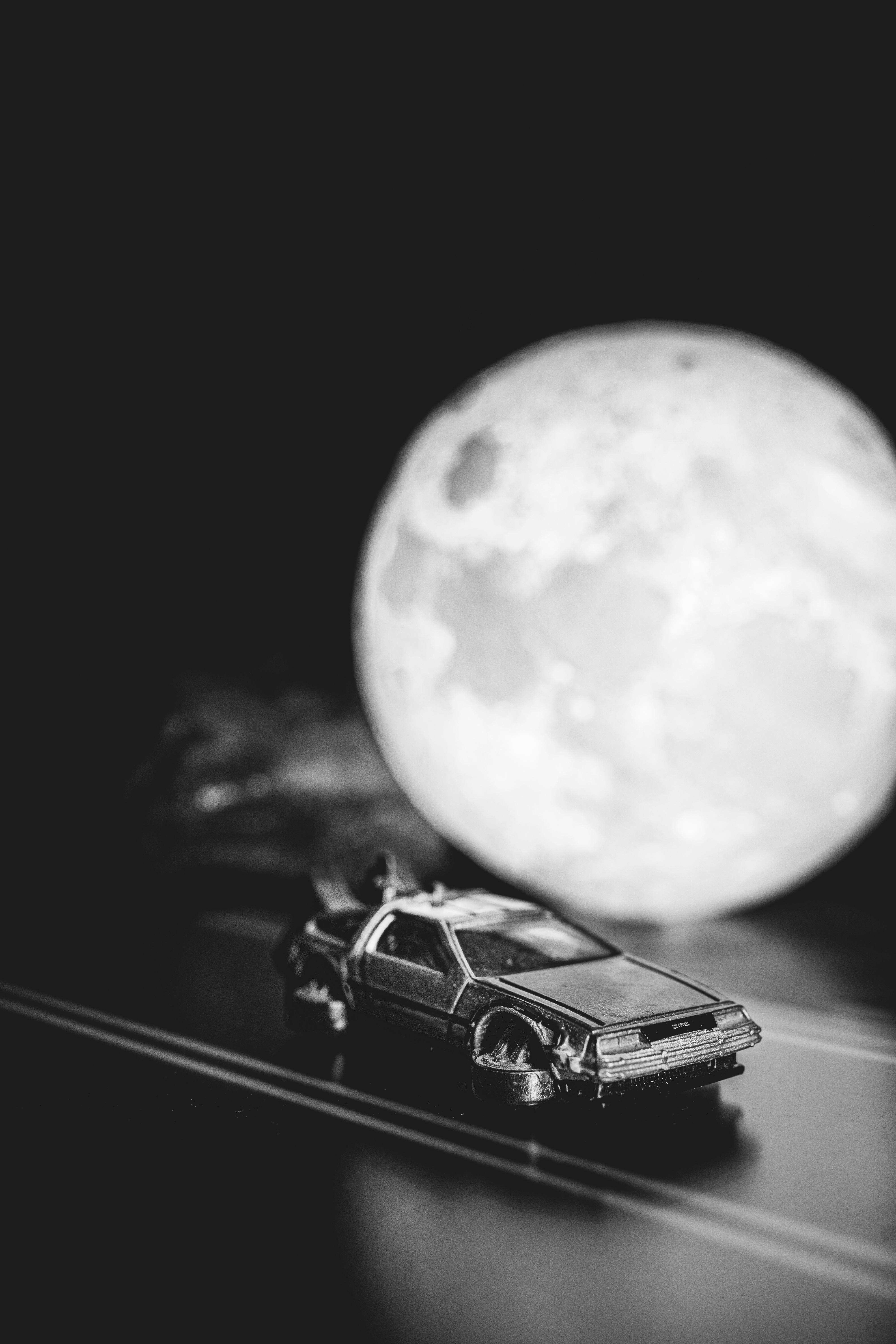 Miniature DeLorean toy on a track with a full moon backdrop in black and white.