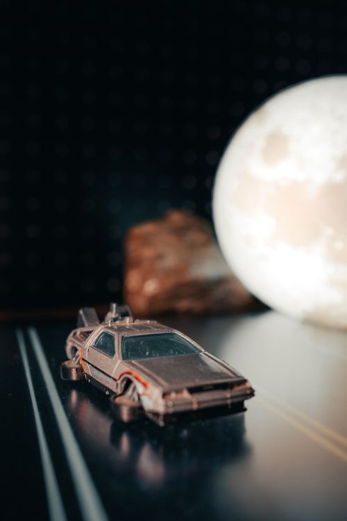 Free A toy car in a futuristic design against a blurred moon backdrop, creating a nostalgic sci-fi atmosphere. Stock Photo