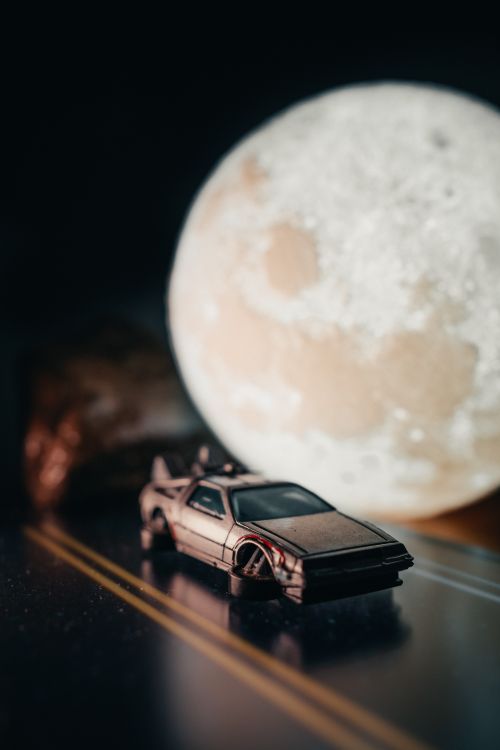 Free A close-up of a toy DeLorean car on a dark road with a large moon backdrop. Stock Photo