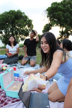 A group of friends having a picnic on a sunny day with sandwiches and drinks, enjoying leisure time outdoors.