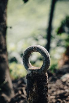 A close-up of a decaying rusty metal ring post outdoors with a blurred nature background.