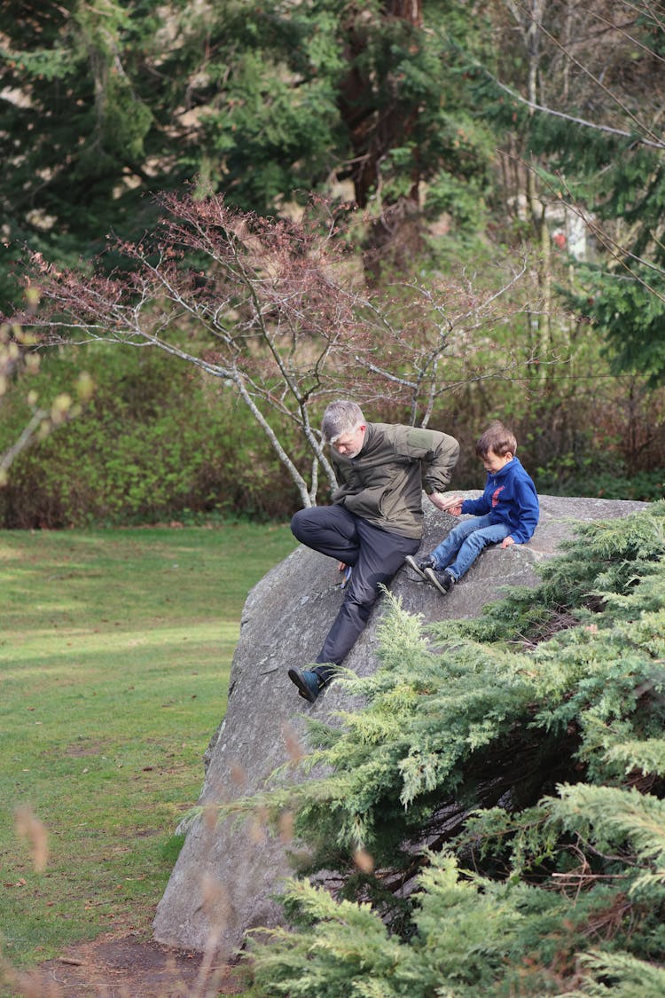 Father And Son Sitting Together On Large Boulder