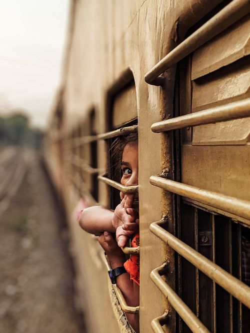 Free A child peeks through a train window, embodying curiosity and travel adventure. Stock Photo