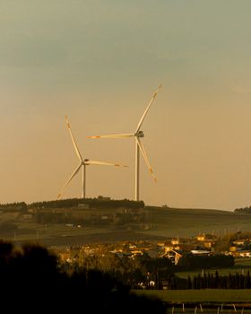 Scenic view of wind turbines on a hill near a rural village, capturing renewable energy beauty.