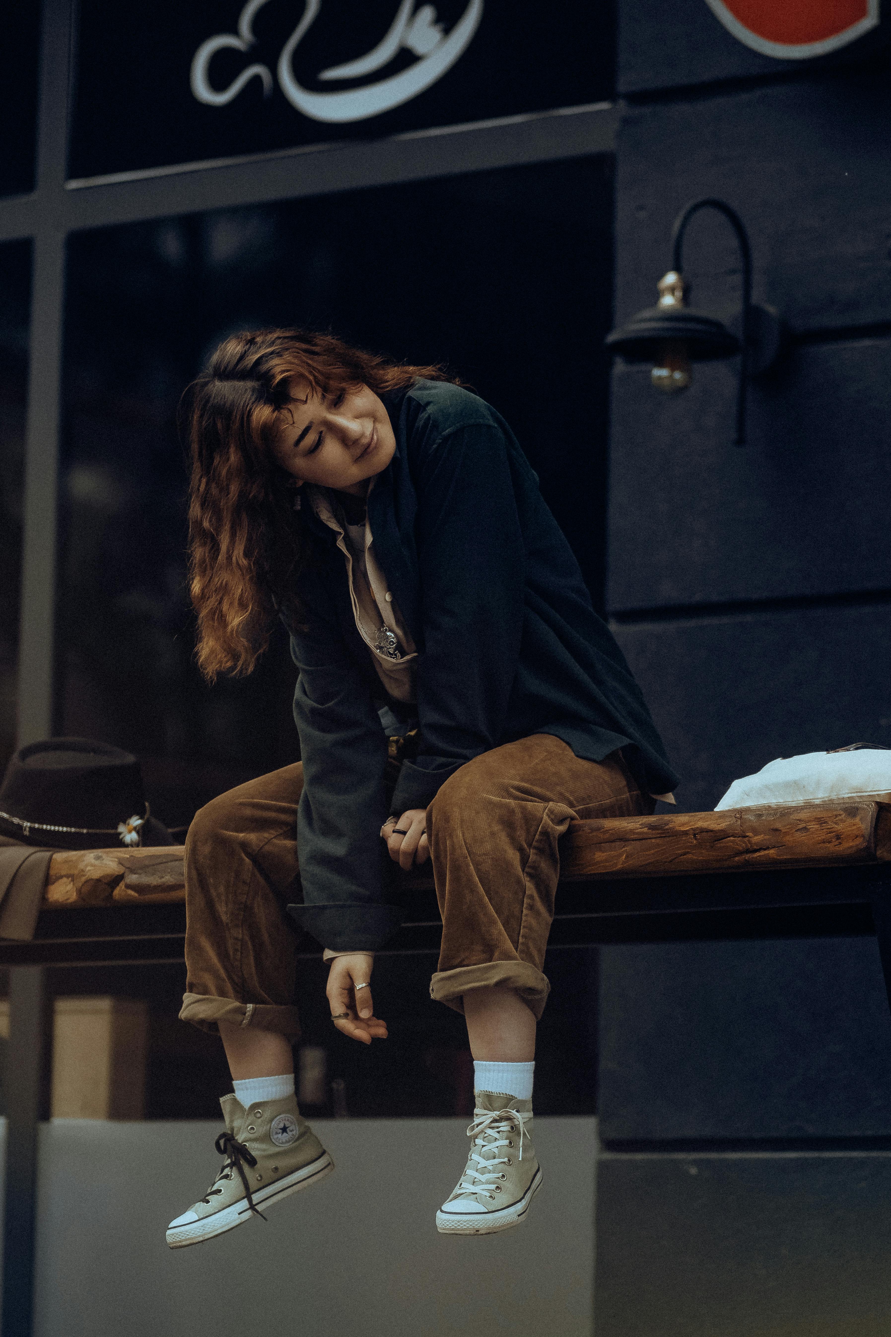 Young woman in casual vintage fashion sitting in urban setting, showcasing relaxed style.