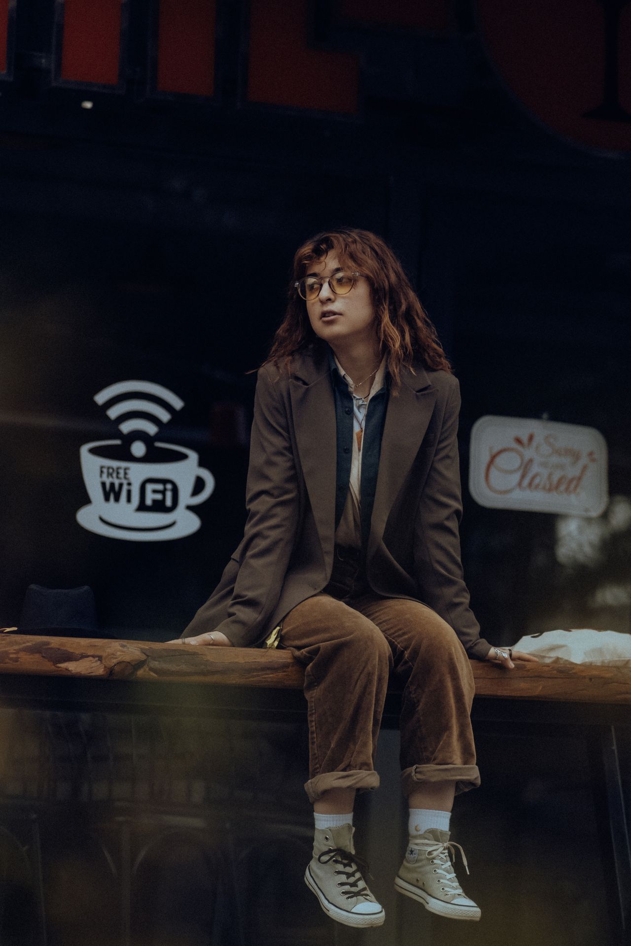 Woman in a brown oversized blazer and matching brown trousers sitting on a ledge at night