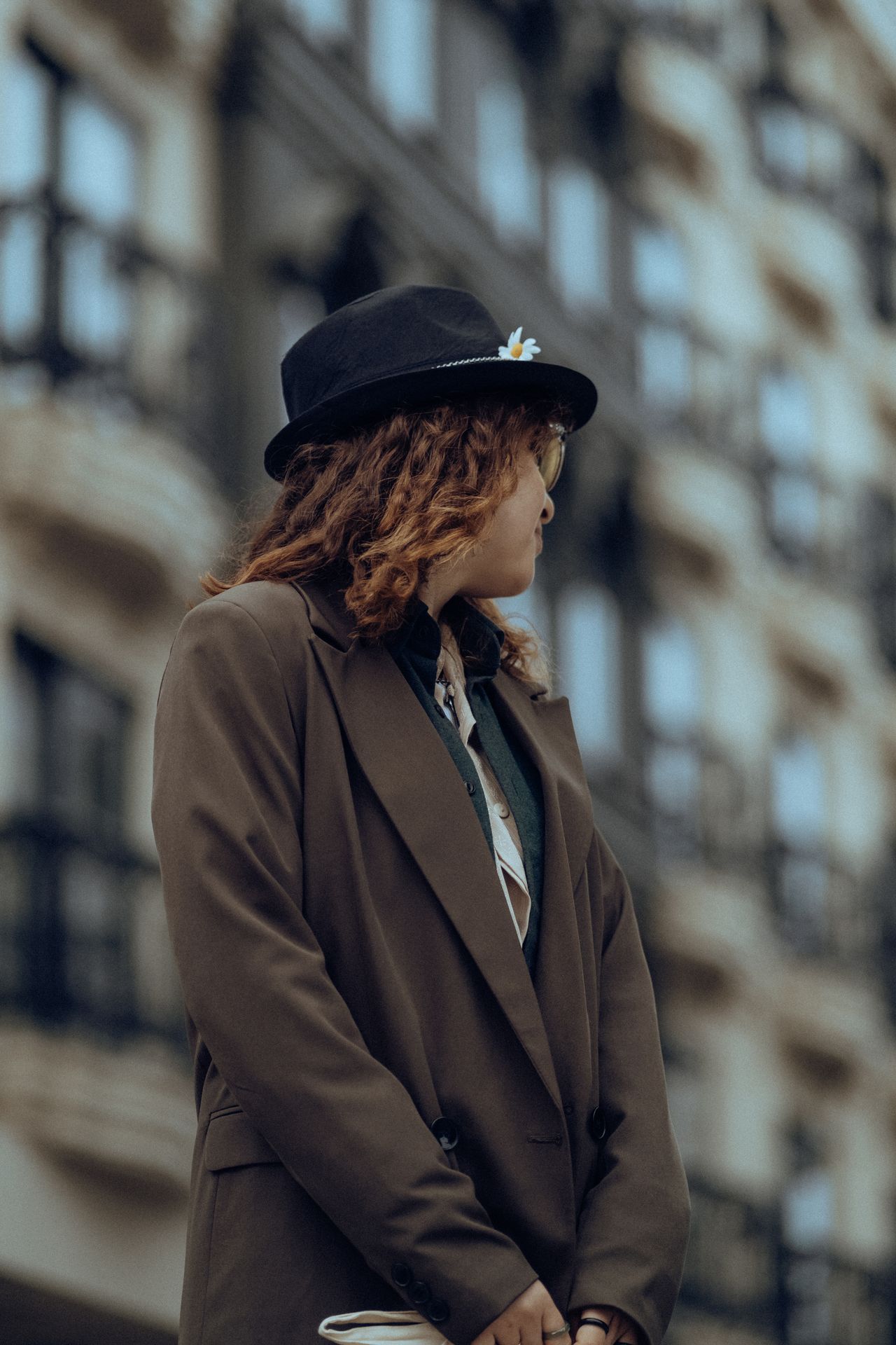 Woman in an oversized brown blazer and black fedora hat on a city street