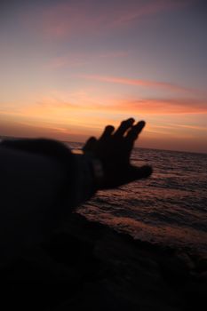 Silhouette of a hand reaching out towards a vibrant sunset over the ocean, capturing the beauty of nature.