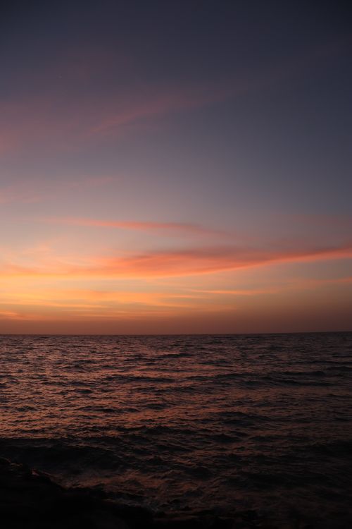 Free A serene sunrise casting vibrant hues over the calm ocean horizon, captured in a vertical shot. Stock Photo
