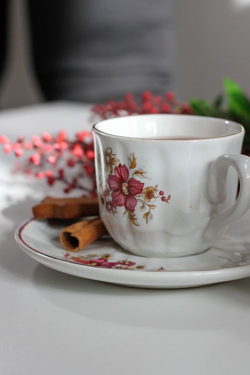 Free A floral teacup filled with tea, adorned with cinnamon sticks and red berries on a table. Stock Photo
