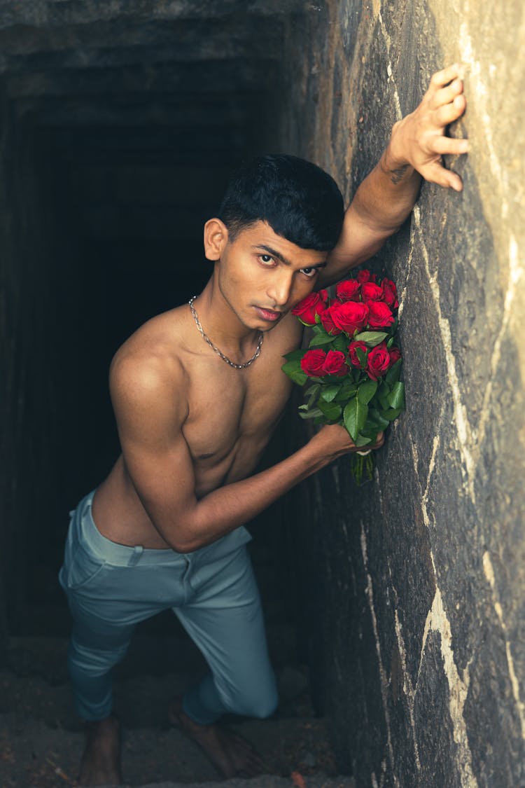 Shirtless Young Man Posing With Bouquet Of Red Roses In Hand In Tunnel