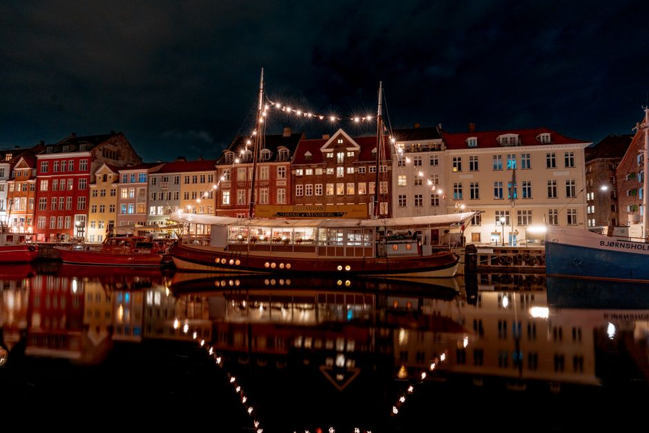 Scenic night view of Nyhavn in Copenhagen featuring illuminated boats and colorful buildings along the canal.